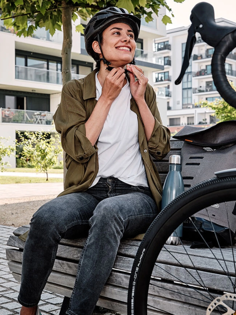 Eine Frau mit Helm sitzt auf einer Bank unter einem Baum Eine Frau mit Helm sitzt auf einer Bank unter einem Baum