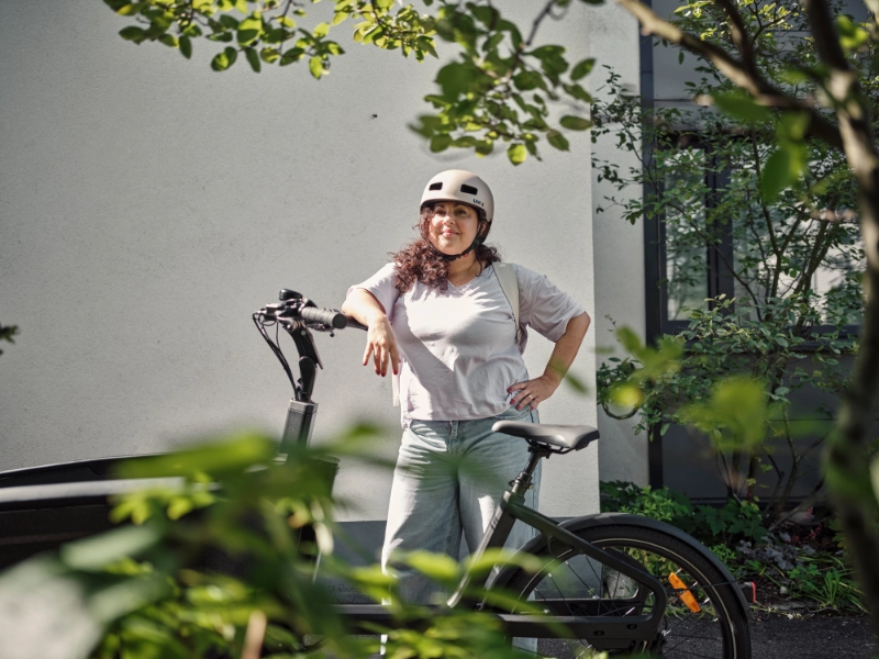 Frau mit Locken lehnt am JobRad, im Vordergrund Pflanzen