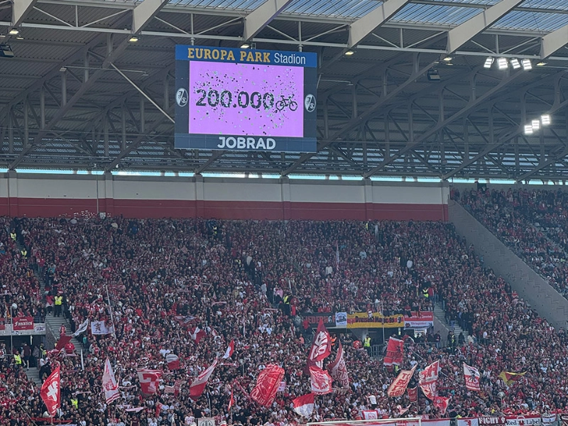 Der Screen im Europa-Park Stadion zeigt an, dass die 200.000 Fahrrad-Fan-Zahl erreicht wurde. Davor sieht man Spieler auf dem Spielfeld.