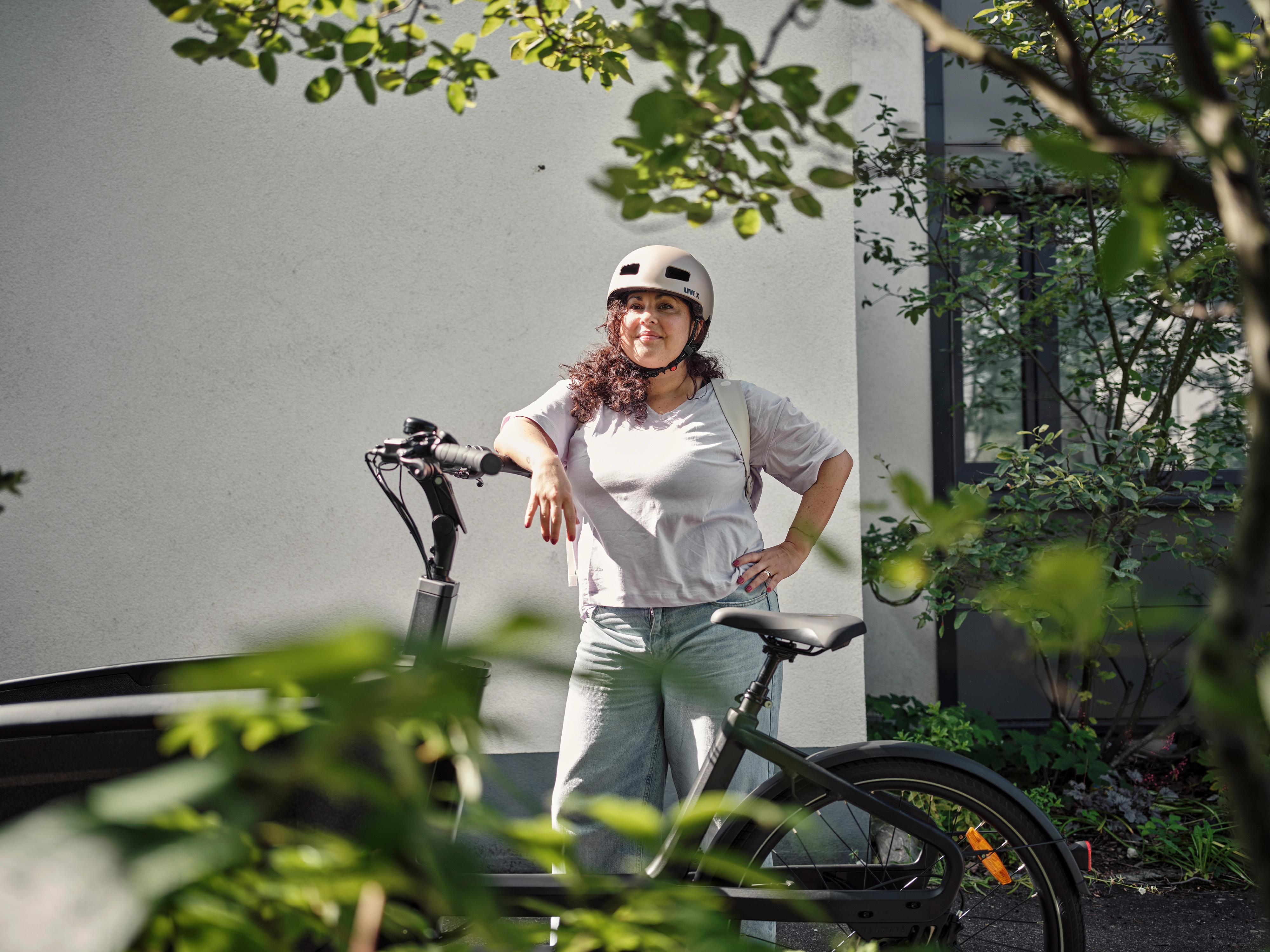 Eine Frau lehnt stolz an ihrem Lastenrad und trägt einen Helm.