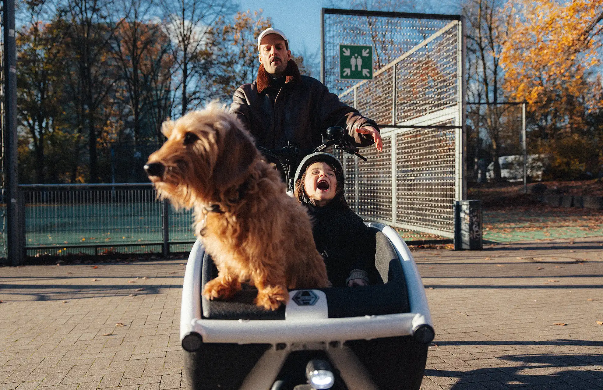 Vater mit lachender Tochter und Hund unterwegs im Lastenrad