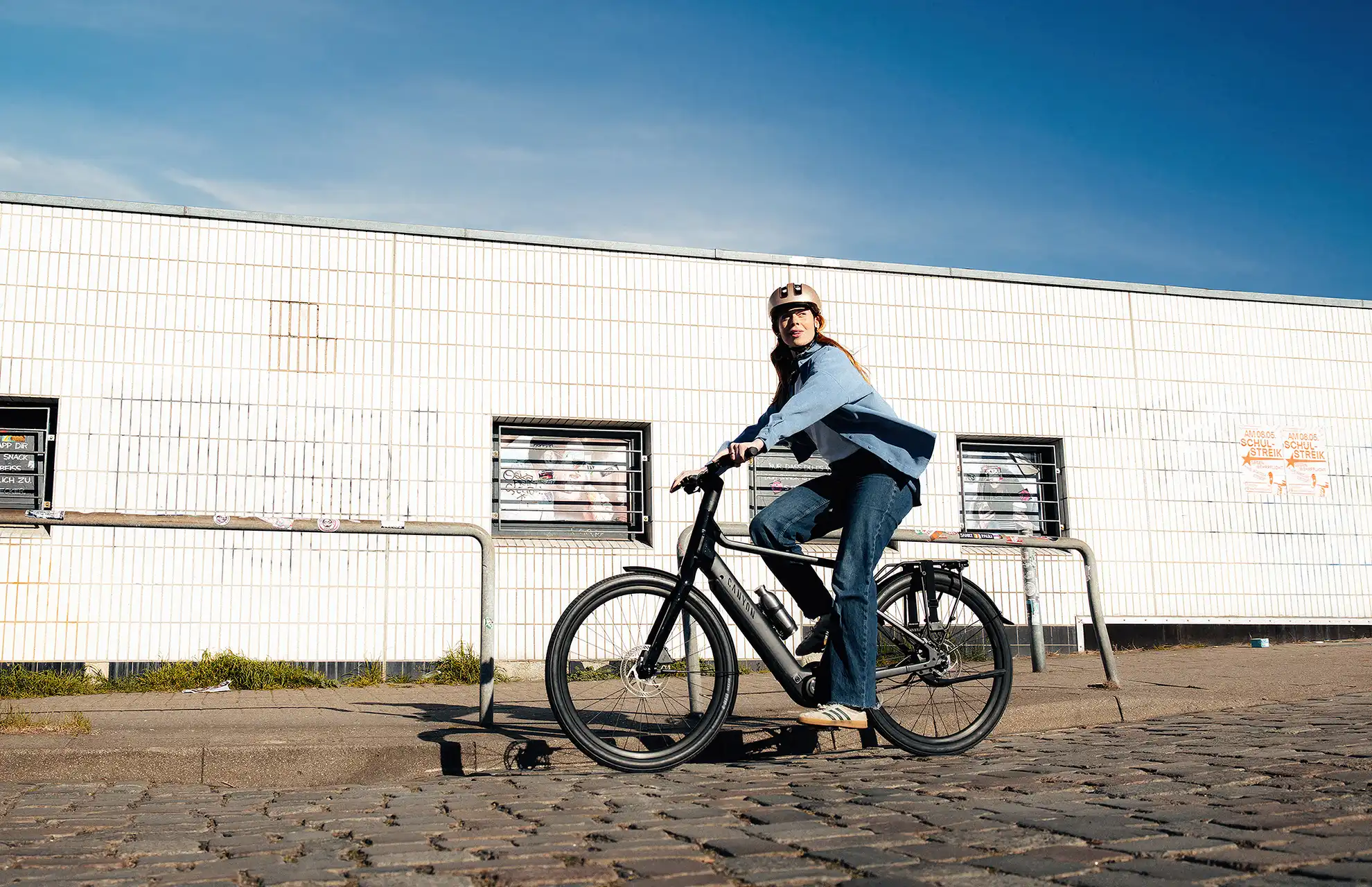 junge Frau auf City E-Bike vor Fabrik mit blauem Himmel im Hintergrund